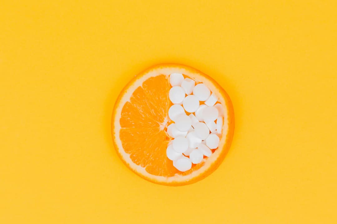 Sliced orange with vitamin tablets filling up half of it on a yellow background