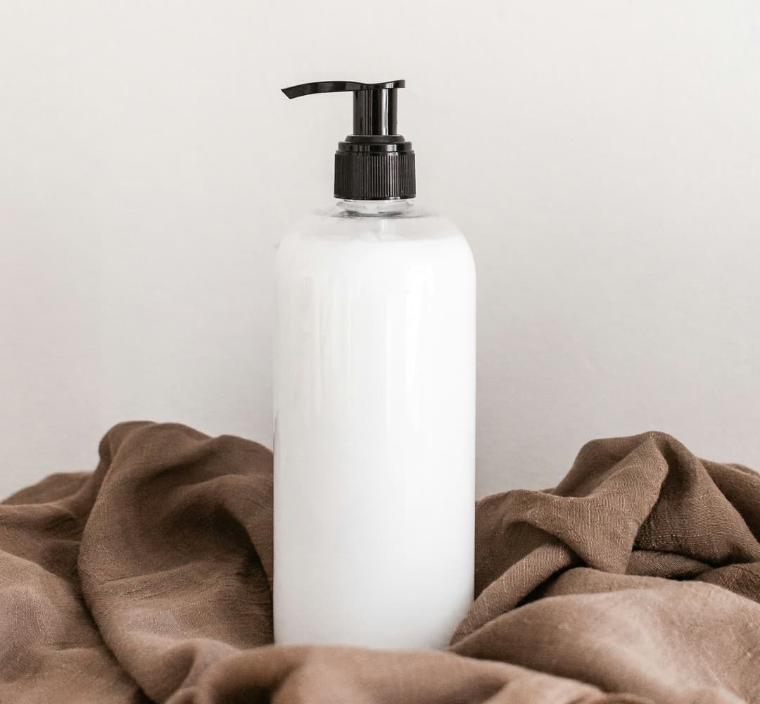 Single bottle of white moisturiser on a brown towel